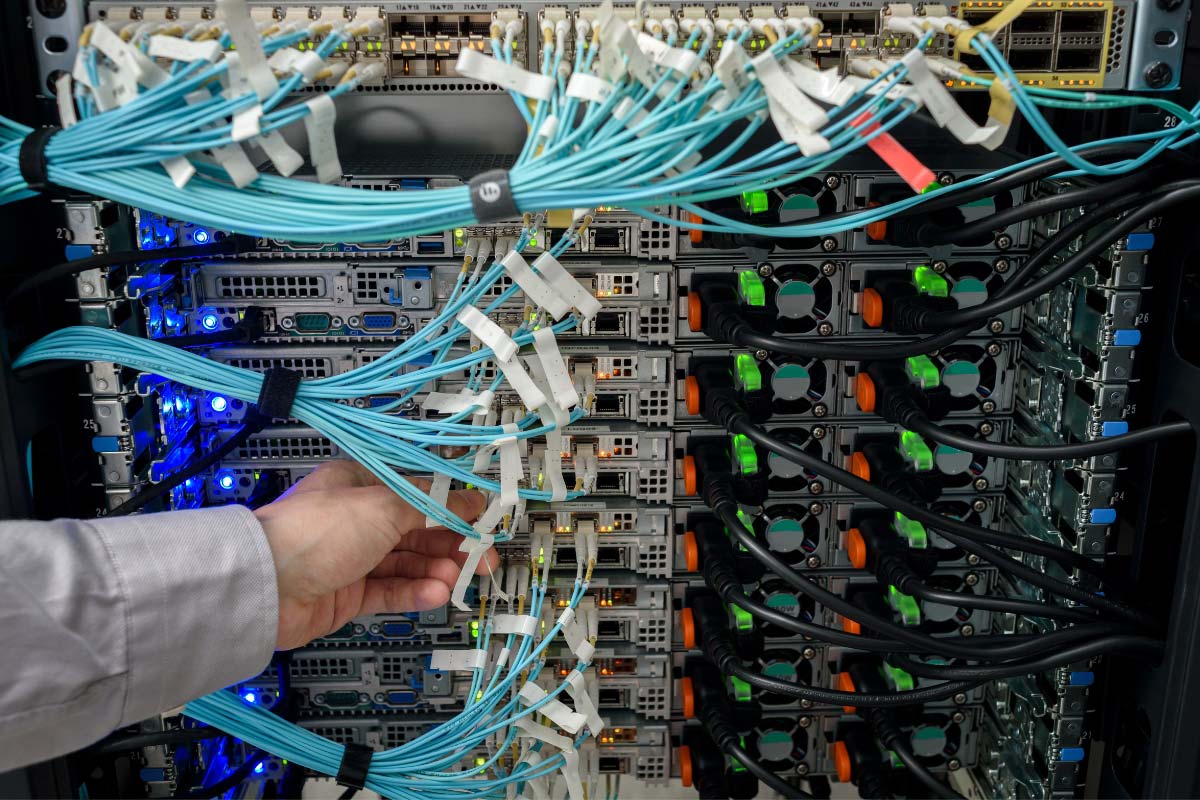 Technician handling labeled cables inside a crowded network rack with servers and patch connections.