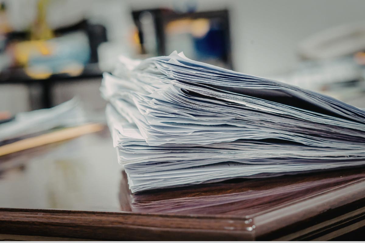 Stack of paper documents on a desk representing project records and closeout paperwork.
