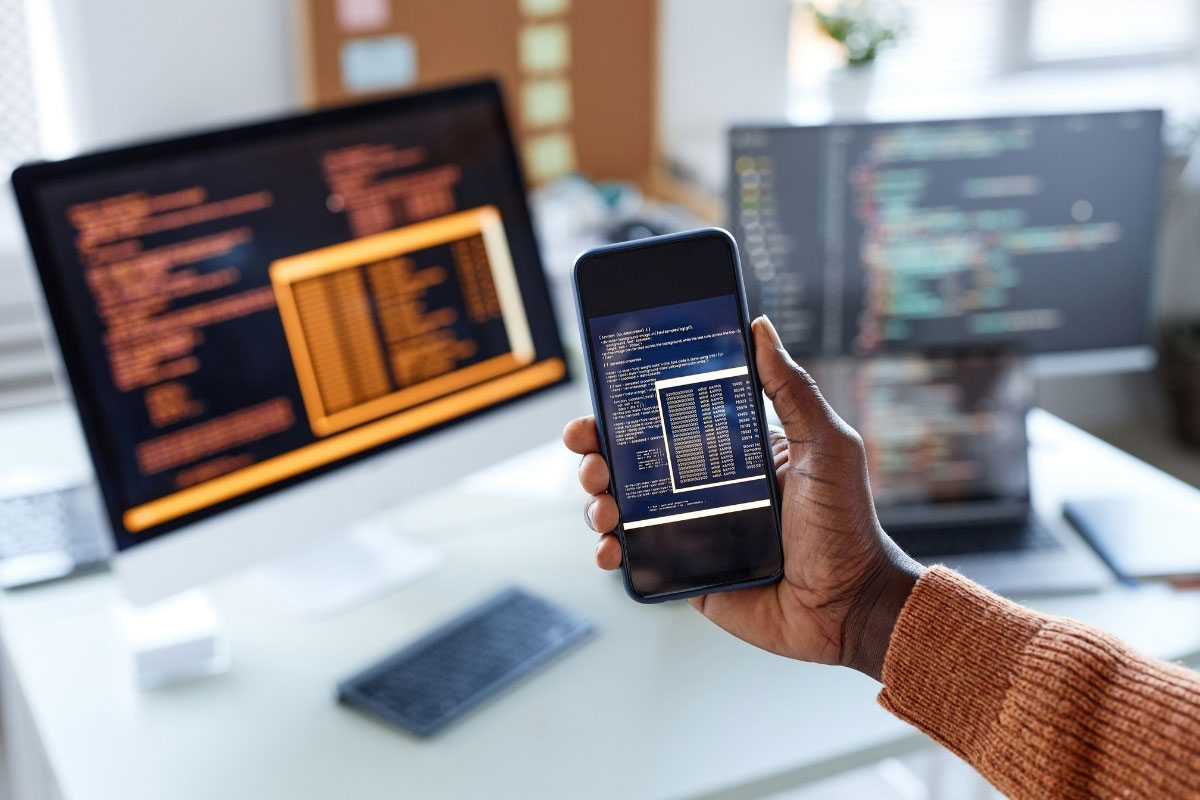 Person testing code on a smartphone and desktop in an office setting